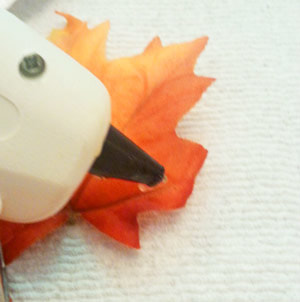Using a hot lue gun to glue leaves together for fall decorations